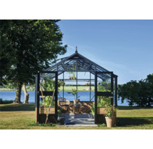 Freistehendes Gewächshaus mit Glaswänden, schwarzem Rahmen und gemauertem Sockel in einem Garten am See.