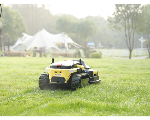 Gelber Mähroboter mit Kettenantrieb bei der Arbeit auf einer weitläufigen grünen Rasenfläche.