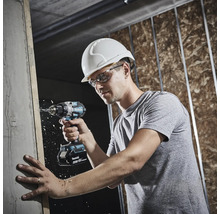 Eine Person mit Schutzhelm und Schutzbrille bohrt mit einem Makita 18 Volt Akkuschrauber auf einer Baustelle in einen Holzbalken.