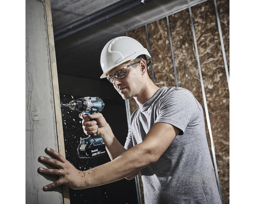 Eine Person mit Schutzhelm und Schutzbrille bohrt mit einem Makita 18 Volt Akkuschrauber auf einer Baustelle in einen Holzbalken.