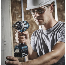 Ein Mann mit weißem Schutzhelm und Schutzbrille verwendet einen Makita 18 Volt Akku-Bohrschrauber, um in ein Holzbrett zu bohren.