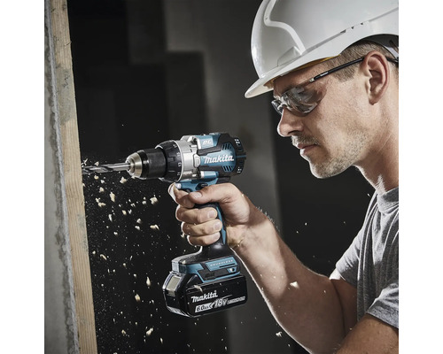 Handwerker mit Schutzhelm und Schutzbrille bohrt mit einem Makita Akku-Bohrschrauber 18 Volt Brushless in ein Holzbrett.
