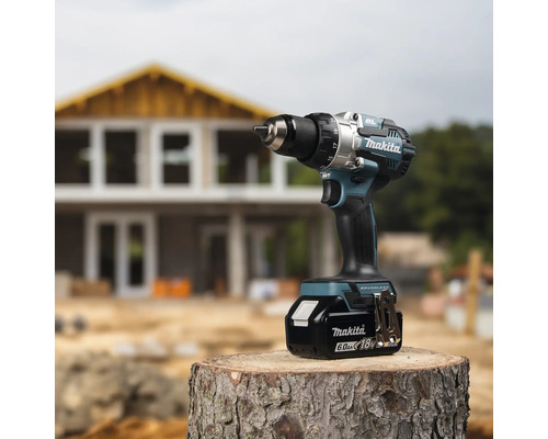 Makita Akku-Bohrschrauber 18 Volt mit 6,0 Amperestunden Akku auf einem Baumstamm vor einer Hausbaustelle.