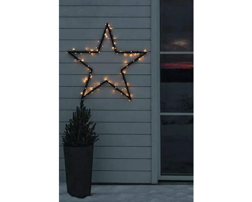 Beleuchteter LED-Stern an einer weißen Holzfassade neben einem kleinen Nadelbaum im Topf bei winterlicher Dämmerung.