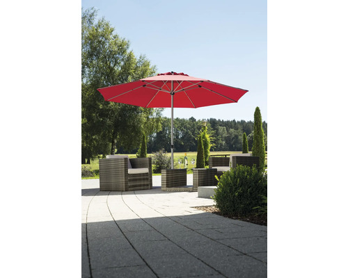 Roter Sonnenschirm über einer Lounge Sitzgruppe aus Polyrattan auf einer gepflasterten Terrasse im Garten.