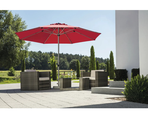 Moderner roter Sonnenschirm über einer Lounge-Sitzgruppe aus Polyrattan auf einer hellen, gepflasterten Terrasse im Garten.