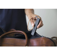 Eine Hand hält einen schwarzen mobilen Sensor mit einer Trageschlaufe über einer braunen Ledertasche.