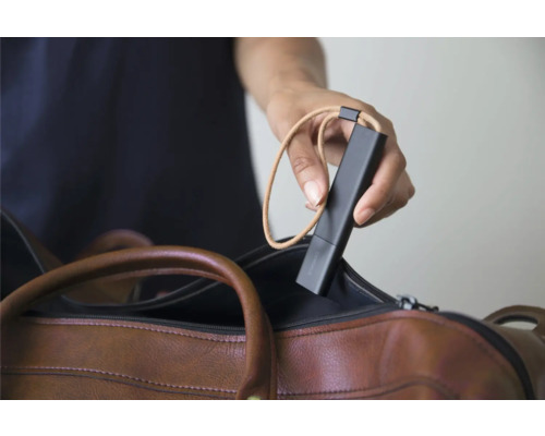 Eine Hand hält einen schwarzen mobilen Sensor mit einer Trageschlaufe über einer braunen Ledertasche.