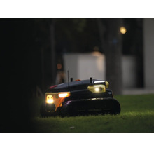 Autonomer Yarbo Gartenroboter auf einer Rasenfläche bei Nacht mit eingeschalteten Scheinwerfern.