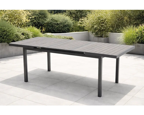 Moderner ausziehbarer Gartentisch aus anthrazitfarbenem Aluminium mit Lattenstruktur auf einer hellen gefliesten Terrasse im Garten.