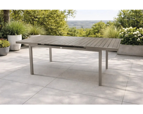 Moderner ausziehbarer Gartentisch aus Metall mit einer Tischplatte in Lattenoptik auf einer hellen Steinterrasse mit grünen Pflanzen.