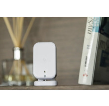 Weißer Smart Home Bewegungsmelder auf einem Regal neben einem Buch und einem Raumduft