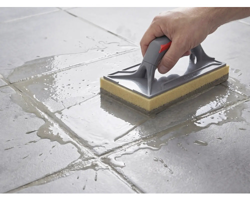 Reinigung von Bodenfliesen mit einem Schwammbrett mit grauem Griff und gelbem Schwammbelag nach dem Verfugen.