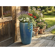 Hoher blauer Keramik-Pflanztopf bepflanzt mit Lavendel und Geranien auf einer Holzterrasse neben einem hölzernen Gartenhaus.