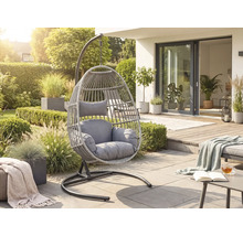 Moderner Hängesessel aus grauem Kunststoffgeflecht mit Polstern auf einer hellen Terrasse in einem sonnigen Garten.