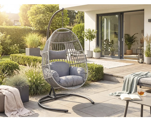 Moderner Hängesessel aus grauem Kunststoffgeflecht mit Polstern auf einer hellen Terrasse in einem sonnigen Garten.