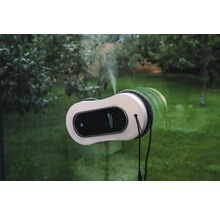 Lifenaxx Fensterreinigungsroboter mit Sprühfunktion reinigt eine Fensterscheibe vor einem Gartenhintergrund.