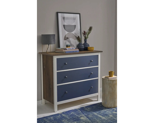 Kommode mit drei blauen Schubladen, weißem Rahmen und Holzoberfläche in einem modern eingerichteten Zimmer.