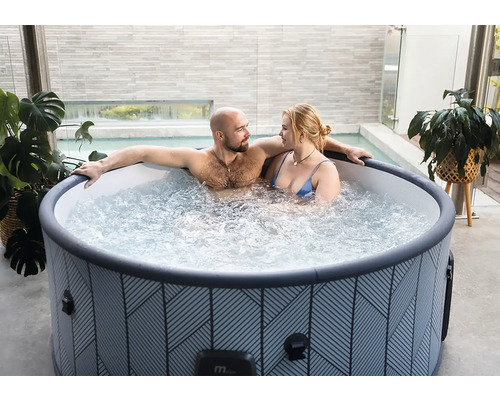 Paar entspannt in rundem, gemustertem aufblasbarem Whirlpool auf einer modernen Terrasse mit Pflanzen.
