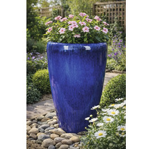 Hoher, blau glasierter Pflanzkübel aus Keramik mit rosa Blüten in einer Gartenumgebung mit Kieselsteinen.