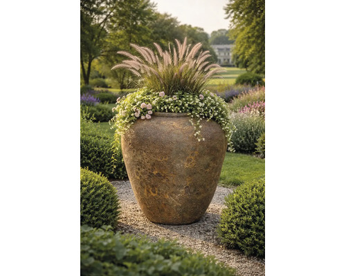 Großer strukturierter Pflanztopf aus Keramik in einem Garten, bepflanzt mit Ziergräsern und Blumen auf einem Kiesweg.