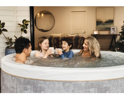 Eine Familie entspannt in einem runden, aufblasbaren Whirlpool mit sprudelndem Wasser in einem gemütlichen Innenraum.