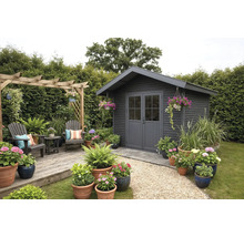 Modernes anthrazitfarbenes Gartenhaus aus Holz mit Doppeltür, Holzterrasse mit Sitzbereich, Pergola und vielen blühenden Topfpflanzen.
