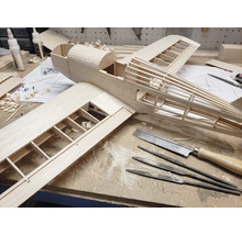 Modellbau eines Flugzeugs aus Holz auf einer Werkbank mit Werkzeugen wie Feinsäge, Nadelfeilen und Holzleim.