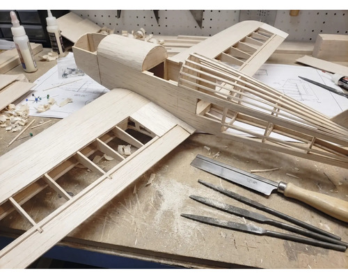 Modellbau eines Flugzeugs aus Holz auf einer Werkbank mit Werkzeugen wie Feinsäge, Nadelfeilen und Holzleim.