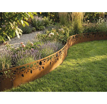 Dekorative Rasenkante aus Metall in Edelrostoptik mit Blumenmuster trennt ein bepflanztes Beet von einer Rasenfläche in einem hellen Garten.