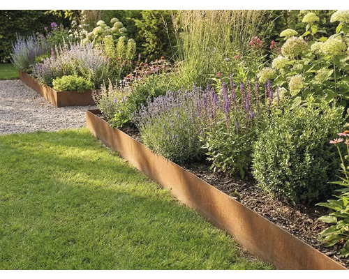 Beetbegrenzung aus Cortenstahl trennt Rasenfläche von einer bepflanzten Rabatte mit Gräsern und Stauden.