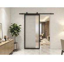 Moderne Schiebetür aus Glas mit schwarzem Metallrahmen und Laufschiene vor einer weißen Ziegelwand in einem hellen Wohnzimmer.