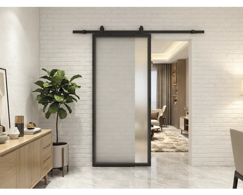 Moderne Schiebetür aus Glas mit schwarzem Metallrahmen und Laufschiene vor einer weißen Ziegelwand in einem hellen Wohnzimmer.