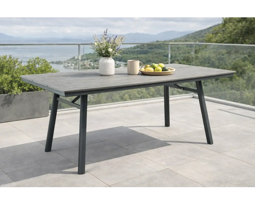 Rechteckiger Gartentisch mit grauer Tischplatte in Holzoptik und schwarzem Metallgestell auf einer hellen, geräumigen Terrasse.