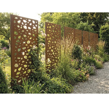 Sichtschutzwand aus Corten-Stahl mit organischem Lochmuster im Garten zwischen Stauden und Gräsern an einem Kiesweg.