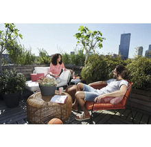 Helle Dachterrasse mit Loungemöbeln, rundem Flecht-Couchtisch, weißem Outdoorsofa, rotem Sessel und vielen grünen Pflanzen wie Bambus.