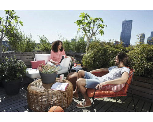 Helle Dachterrasse mit Loungemöbeln, rundem Flecht-Couchtisch, weißem Outdoorsofa, rotem Sessel und vielen grünen Pflanzen wie Bambus.