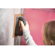 Hand glättet eine Wand mit einem Kunststoff-Reibebrett und trägt eine Grundierung auf.