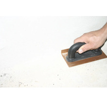 Hand führt eine Inneneckenkelle aus Metall mit schwarzem Griff beim Verputzen einer Wand.