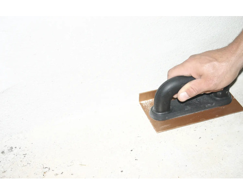 Hand führt eine Inneneckenkelle aus Metall mit schwarzem Griff beim Verputzen einer Wand.