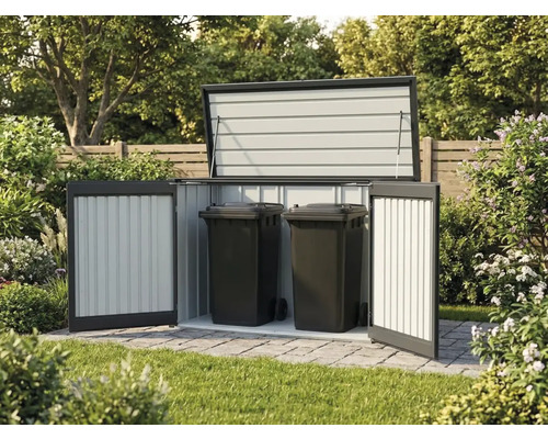 Geöffnete Mülltonnenbox aus Metall mit zwei schwarzen Mülltonnen auf gepflasterter Fläche im Garten.