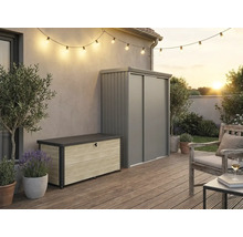 Außenbereich mit moderner Aufbewahrungsbox in Holzoptik und grauem Metall-Gartenschrank auf einer Holzterrasse mit Lichterkette und Sitzbereich.
