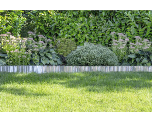 Rasenkante aus Metall trennt die Rasenfläche von einem Beet mit Stauden und Sträuchern vor einer Hecke.