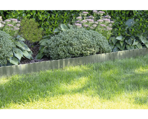 Wellenförmige Rasenkante aus Metall trennt eine Rasenfläche von einem Gartenbeet mit verschiedenen Pflanzen und Sträuchern.