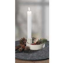 Brennende weiße Stabkerze in weißem Halter, dekoriert mit Tannenzapfen, Rinde und Tannenzweig auf grauem Filzuntersetzer.