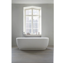 Freistehende weiße Badewanne in modernem hellem Badezimmer vor einem Fenster, bodenstehende Armatur, Holzfußboden.