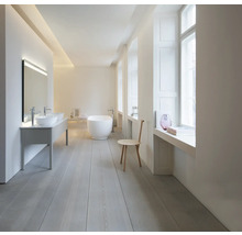 Helles, minimalistisches Badezimmer mit freistehender weißer Badewanne, Doppelwaschtisch mit Aufsatzbecken und hellem Holzboden.