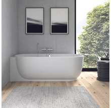 Moderne Badewanne vor Betonwand mit verchromter Wandarmatur, Holzboden und großem Fenster mit Blick in den Garten.
