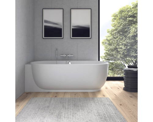Moderne Badewanne vor Betonwand mit verchromter Wandarmatur, Holzboden und großem Fenster mit Blick in den Garten.