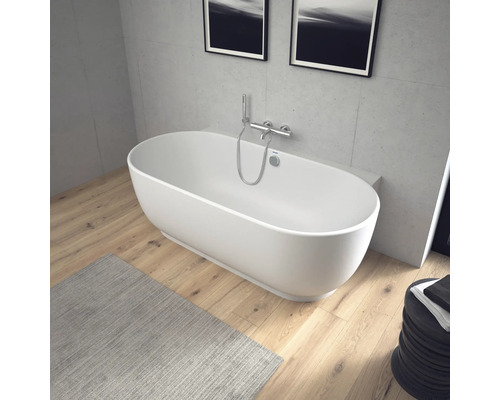 Freistehende ovale Badewanne mit wandmontierter Chrom-Armatur in einem modernen Badezimmer mit Holzboden und Wänden in Betonoptik.